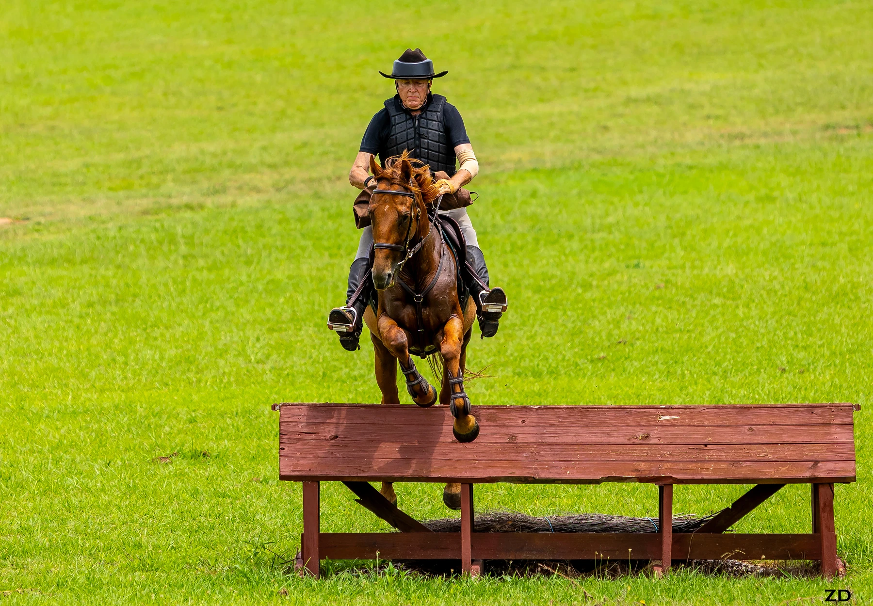 Equestrian jumping over wooden obstacle outdoors.