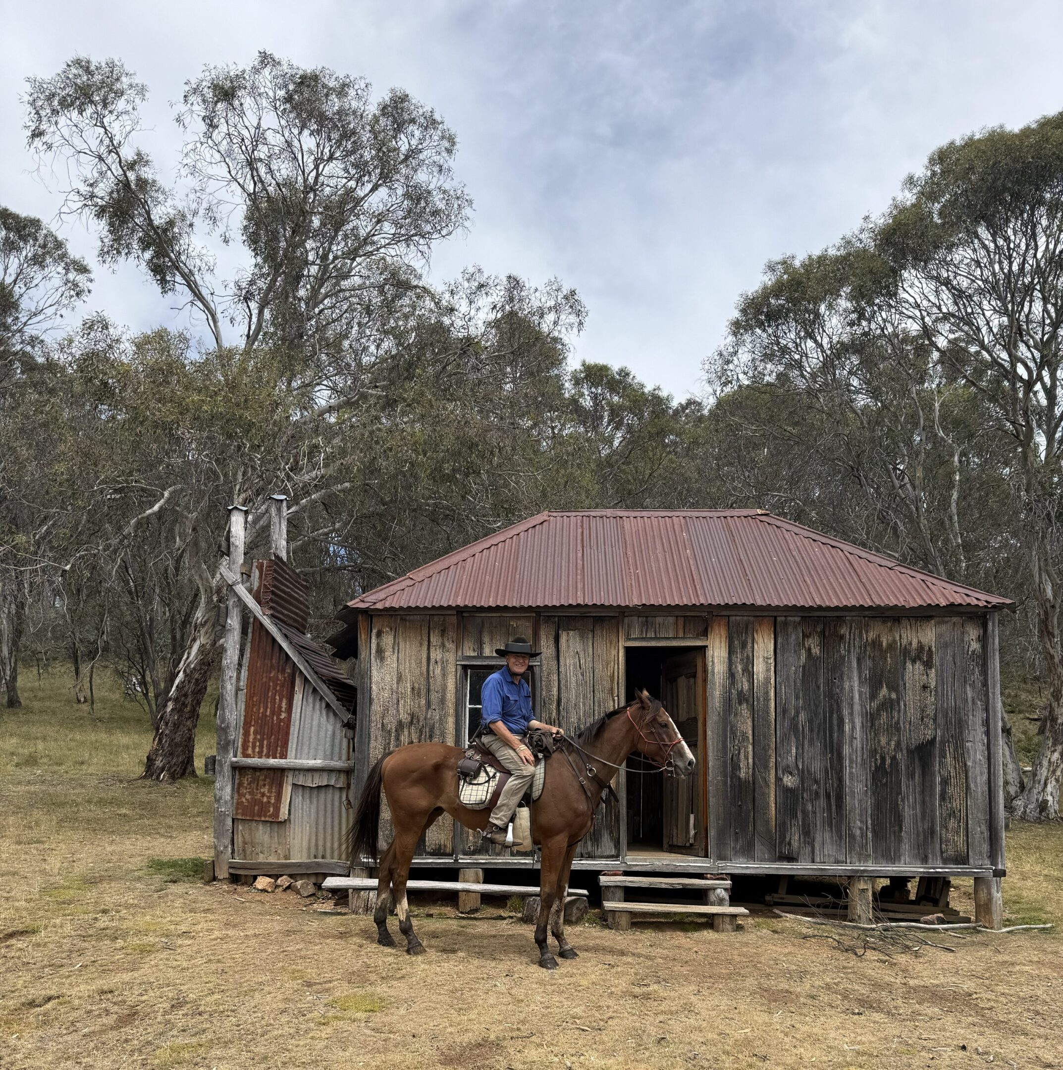 Man on horseback in front of rustic cabin